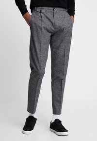 Grå mønstrede bukser med en skræddersyet pasform, der har en glat front, lommer og manchetter, parret med sorte sneakers og hvide sokker.