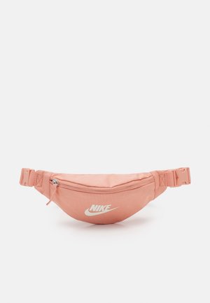 Sac banane Nike rose avec logo blanc, poche avant zippée et sangle latérale réglable avec boucle sur fond uni.