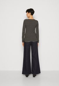 Schwarz-weiß gestreiftes Langarmoberteil kombiniert mit hoch taillierten, weit geschnittenen, dunklen Jeans. Das Ensemble zeichnet sich durch eine figurbetonte Silhouette und weite Beine aus.