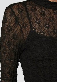 Zwarte kanten top met geprinte doorschijnende lange mouwen, een aansluitend lijfje en een textiel met een bloemenpatroon.