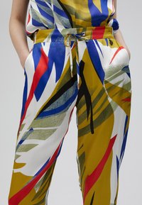 Pantaloni con un vivace motivo multicolore caratterizzato da grosse forme a foglia in blu, rosso, verde e giallo su uno sfondo bianco.