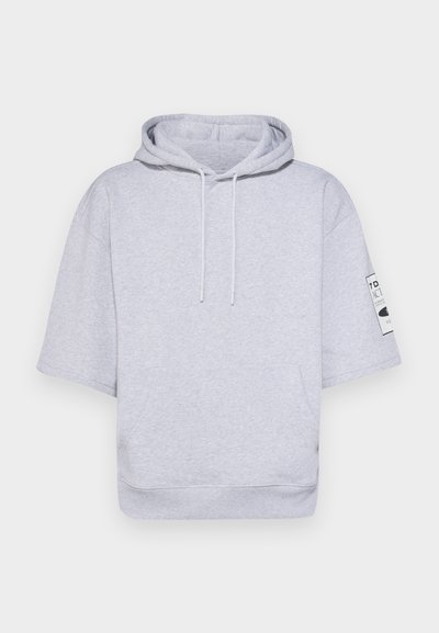 Hanorac scurt de culoare gri deschis, confecționat dintr-o stofă moale, având glugă cu șnur, mâneci scurte și un patch cu etichetă pe brațul stâng.