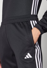 Schwarzer Sporttracksuit mit weißen Drei-Streifen-Accents, elastischem Bund und Seitentasche, aus glattem, atmungsaktivem Stoff gefertigt.