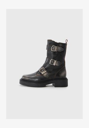 Black leather ankle boot with three metallic buckles, round toe, matte finish, and a thick rubber sole. Features a pull tab at the back.
