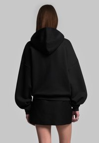 Felpa nera oversize con cucitura sul retro e cappuccio, abbinata a una gonna nera aderente. Tessuto morbido con dettagli a coste nei polsini e all'orlo.