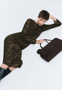 Vestido largo y ajustado de material translúcido en tono marrón con un patrón de rayas de tigre negras. La modelo sostiene un bolso de ante marrón oscuro. Las botas presentan una textura brillante.