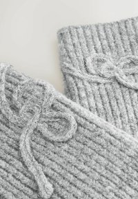 Grau gestrickte Accessoires mit einem gerippten Textur. Enthält gebundene weiche Garnakzente für den Verschluss, die Wärme und ein gemütliches Erscheinungsbild zeigen.