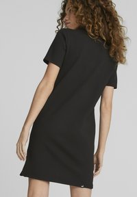 Melnas īsām piedurknēm kleita ar teksturētu audumu, taisns griezums un logotipa akcents apakšmalā, attēlota no leņķa aizmugures skata.