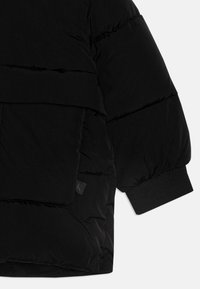 Puffjakke i svart, med tykk, quiltet design, stor frontlomme, ribbestrikkede mansjetter og en glatt ytre tekstur.