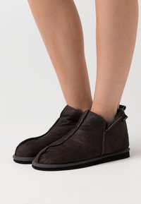 Donkerbruine enkellaarzen van zacht suède, met een gestikt randje, een grijze voering en een platte zool met een subtiele hak.
