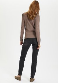 Brun långärmad stickad tröja med ribbad nederkant, i kombination med mörka skinny jeans och bruna mockaskor, sett bakifrån.