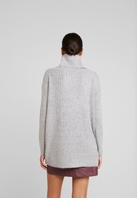 Maglione grigio lavorato a maglia con colletto alto a coste e vestibilità rilassata. Presenta maniche lunghe e un motivo testurizzato.