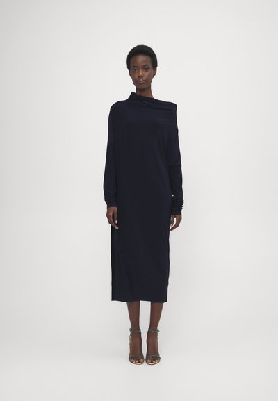 Rochie bleumarin cu mâneci lungi, guler drapat, croi lejer și fanta laterală. Material neted și design lungime ankle. Asortată cu sandale cu bretele.