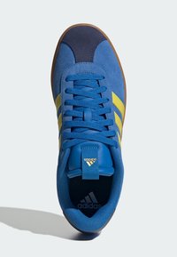 Scarpa sportiva blu scamosciata con strisce gialle, puntale blu navy e interno testurizzato nero. Presenta lacci piatti blu e il logo Adidas.