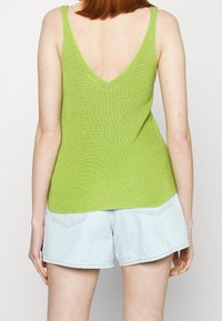 Grön stickad linne med V-baksida, med en texturerad yta. Matchat med ljusblå denimshorts, vilket visar en avslappnad outfit.