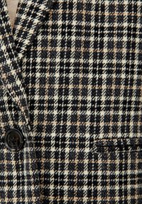 Blazer a quadri con una combinazione di tonalità nere, beige e marrone chiaro. Tessuto testurizzato con un singolo bottone nero e un dettaglio con tasca laterale.