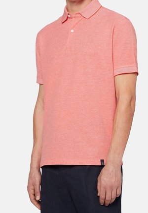 Jasnoróżowa koszulka polo z teksturowanej tkaniny, z kołnierzykiem zapinanym na guziki, krótkimi rękawami oraz małą metką marki przy dolnym końcu.