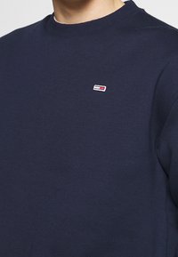 Sudadera de color azul marino hecha de una tela suave, con un escote redondo y un pequeño logo bordado en rojo, blanco y azul en el pecho.