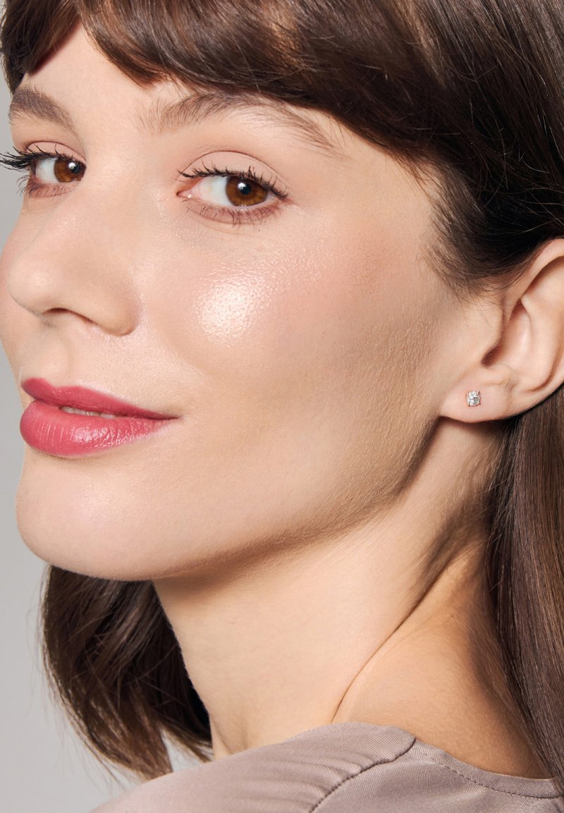 Delikatne kolczyki wkrętki z przezroczystymi kamieniami osadzonymi w metalowej oprawie w srebrnym odcieniu, noszone przez modelkę z gładką skórą i neutralnym kolorem ust.