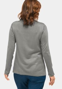 Graues Langarmshirt mit glatter Textur und abgerundetem Saum. Hat ein schlichtes Design und wird mit blauen Jeans kombiniert.