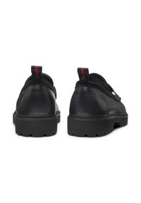 Scarpe in pelle nera con finitura testurizzata, forma arrotondata, suole spesse in gomma nera e marchio rosso sulle linguette posteriori.