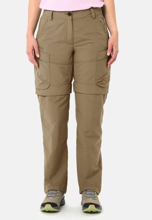 Persoon die beige om te bouwen cargobroek en wandelschoenen draagt, staand tegen een effen witte achtergrond.