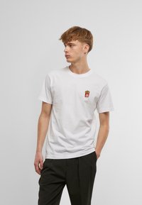 Hvid bomulds t-shirt med et lille broderet motiv af pomfritter i en rød beholder på venstre bryst. Rund hals, korte ærmer.