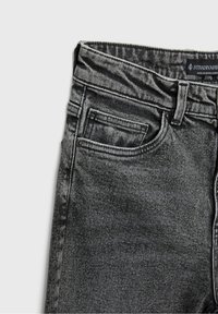 Jeans de mezclilla negra con un lavado desgastado, diseño de cinco bolsillos, costuras visibles y cierre de botón metálico. La tela tiene una textura suave.
