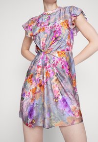 Robe florale avec des manches courtes à volants, présentant un fond violet clair orné de motifs de fleurs orange, rose et verte vibrants.