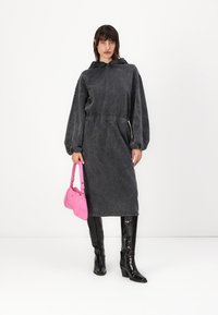 Gray denim long-sleeve dress with a hood, elastic waist, and side pockets, paired with glossy black knee-high boots and a pink handbag.
