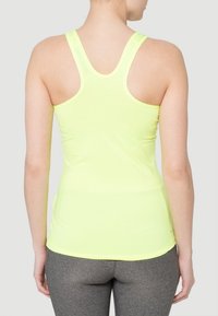 Débardeur de sport jaune vif avec un dos nageur, fabriqué en matériau léger. Style ajusté, associé à des leggings gris.