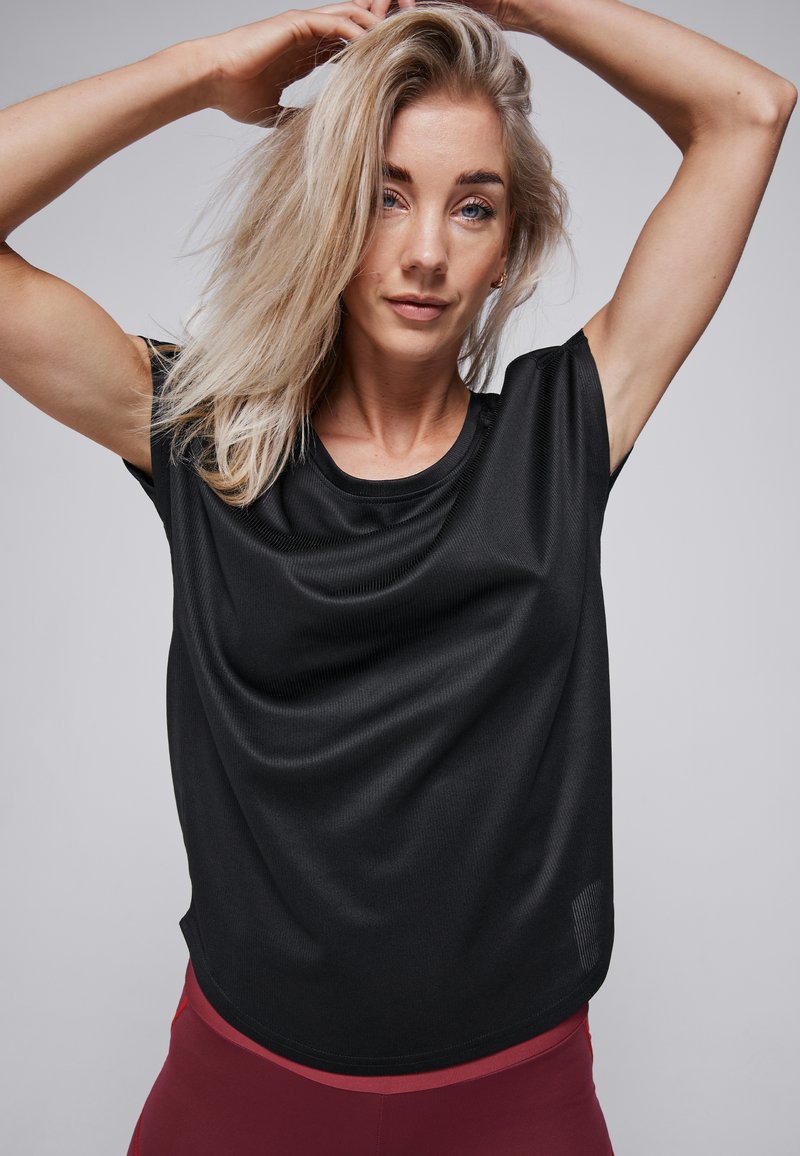 Zwarte sport t-shirt met korte mouwen, een gladde textuur, een ronde halslijn en een subtiele glans, gecombineerd met rode trainingsleggings.
