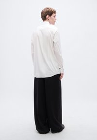 Λευκό πουκάμισο με μακριά μανίκια και ίσια κοπή, συνδυασμένο με φαρδιά μαύρη παντελόνια, με υφή απαλού υφάσματος και κλασικό σχέδιο για το γιακά.