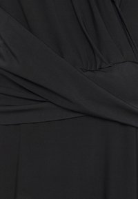 Černé šaty vyrobené z hladkého materiálu, s volným střihem, nařasením v pase a dlouhými rukávy.