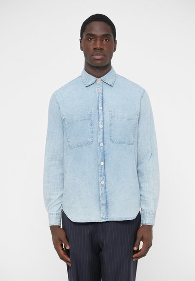 Chemise en denim bleu clair à manches longues, boutonnée sur le devant, avec deux poches poitrine et un col classique. Texture lisse et coupe décontractée.