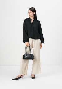 Black button-up shirt with long sleeves, cream pleated wide-leg pants, pointed black slingback shoes, and a small black handbag.