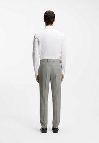 Biała koszula z długim rękawem i szare, dopasowane spodnie garniturowe z fakturą, o wąskim kroju, czarne buty, widziane od tyłu.