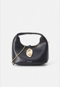 Mustasta nahasta valmistettu pyöreämuotoinen käsilaukku, jossa on kullanvärinen koristus ja ketjuhihna. Logokuva etuosassa. Sileä pinta.