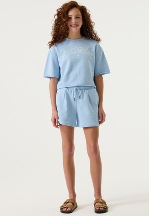 Camiseta de algodón azul claro con la palabra "SUNSET" impresa en blanco, combinada con pantalones cortos a juego que cuentan con una cintura elástica y cordón ajustable.