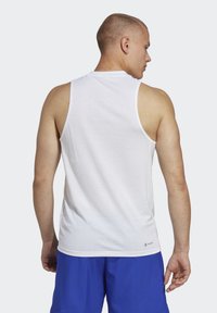 Hvid ærmeløs tanktop med en glat tekstur, rund halsudskæring og hvid kant. Båret med blå shorts. Logo nederst til venstre.
