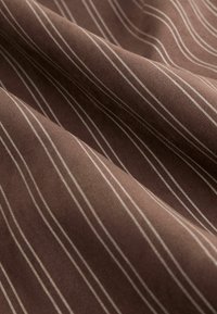 Tissu brun avec de fines rayures blanches verticales. La texture semble douce et légèrement drapée, mettant en valeur le tissage lisse du tissu.
