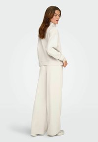 Lys beige loungewear sæt bestående af en pullover med høj krave og brede bukser lavet af blødt stof, med en afslappet pasform og minimalistisk design.
