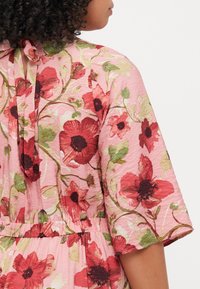 Floral dress featuring a pink base with red and green flower patterns, short sleeves, a relaxed fit, and a tie closure at the back.