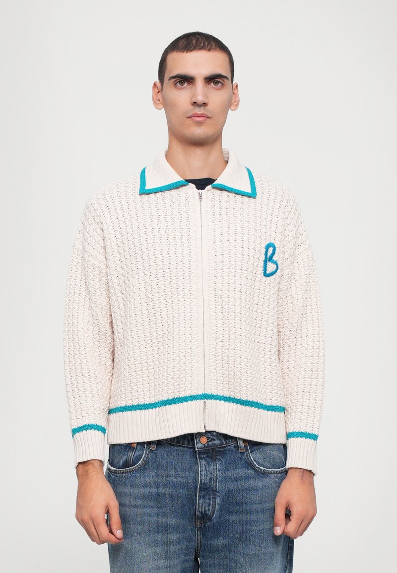 Light beige zip-up sweater with a textured weave. Features a teal collar and lower band, plus a stitched blue letter "B" on the left chest.