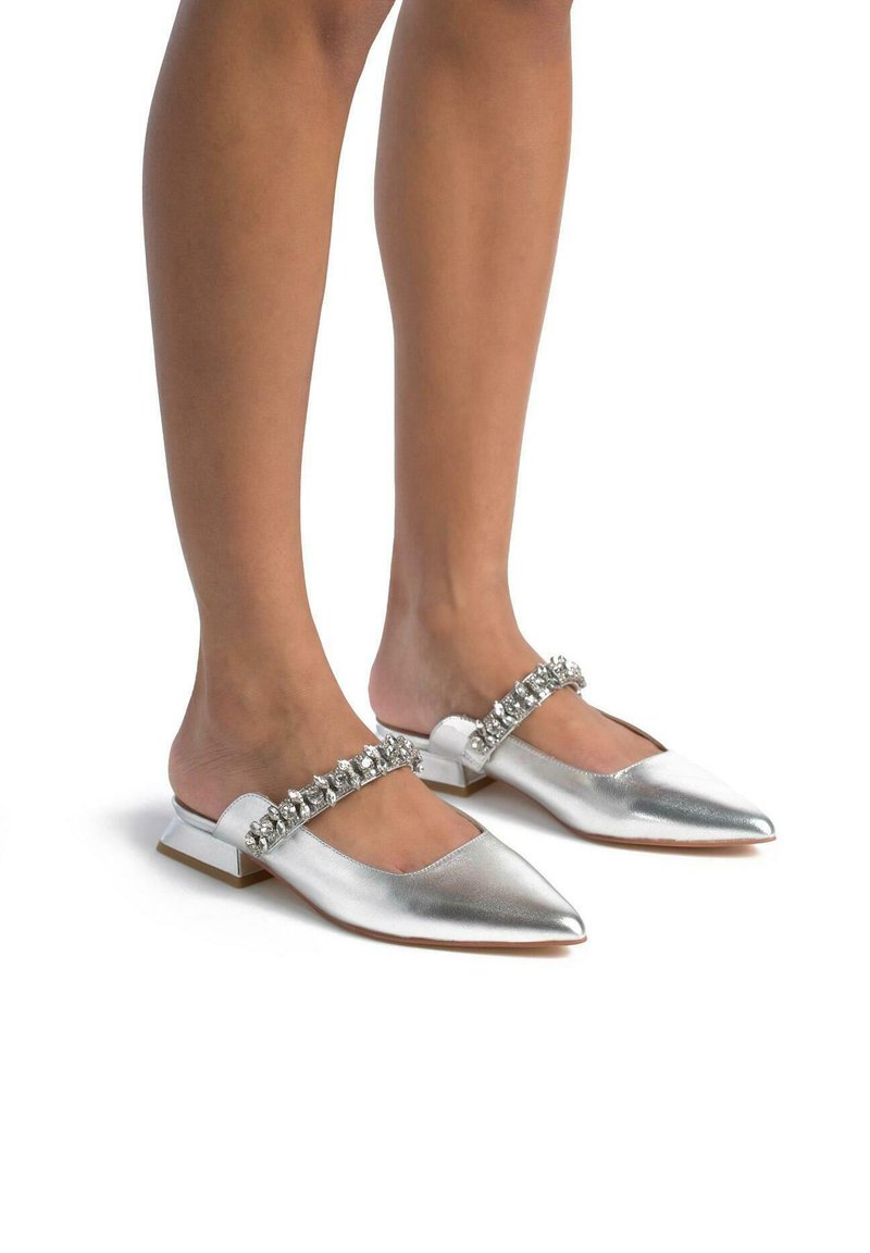 Scarpe slip-on metalliche argentate con punta affusolata e tacco a blocco piccolo, dotate di una fascia decorata con cristalli che attraversa la parte anteriore.