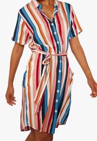 Donna che indossa un vestito di lunghezza al ginocchio, con maniche corte e bottoni davanti, caratterizzato da strisce verticali multicolori e una cintura annodata in vita.