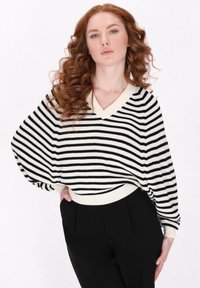 Maglione a righe bianche e nere con scollo a V e maniche a goccia. Realizzato in morbido materiale a maglia con polsini e vita a coste.