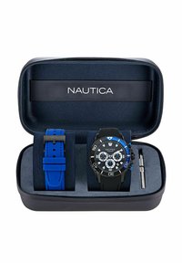Set de reloj Nautica en una caja negra. Presenta un reloj negro con acentos azules y una correa de silicona azul, junto con una correa azul adicional.