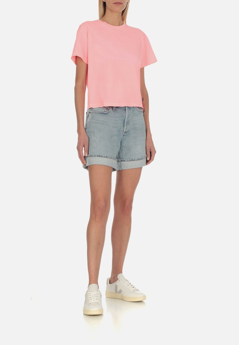 T-shirt rose cropped, à manches courtes, associé à un short en denim bleu clair avec des revers, complété par des baskets blanches.