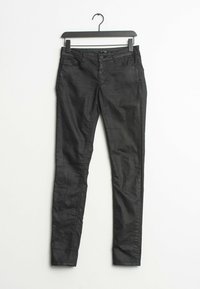 Jean skinny noir avec une texture lisse, cinq poches et une fermeture à bouton. Suspendu à un cintre en plastique noir sur fond blanc.